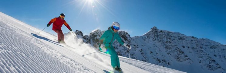 Picture of two people skiing down the mountain in the sun